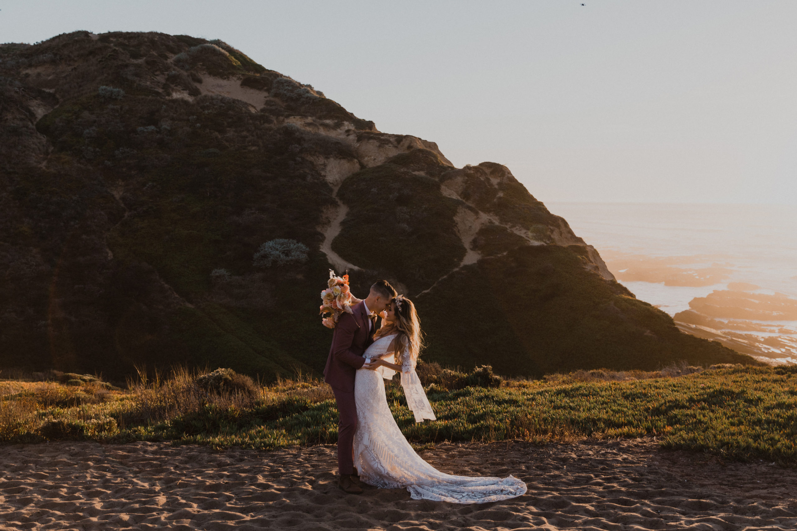 bride and groom in boho elopement embrace on a cliff on the california coast