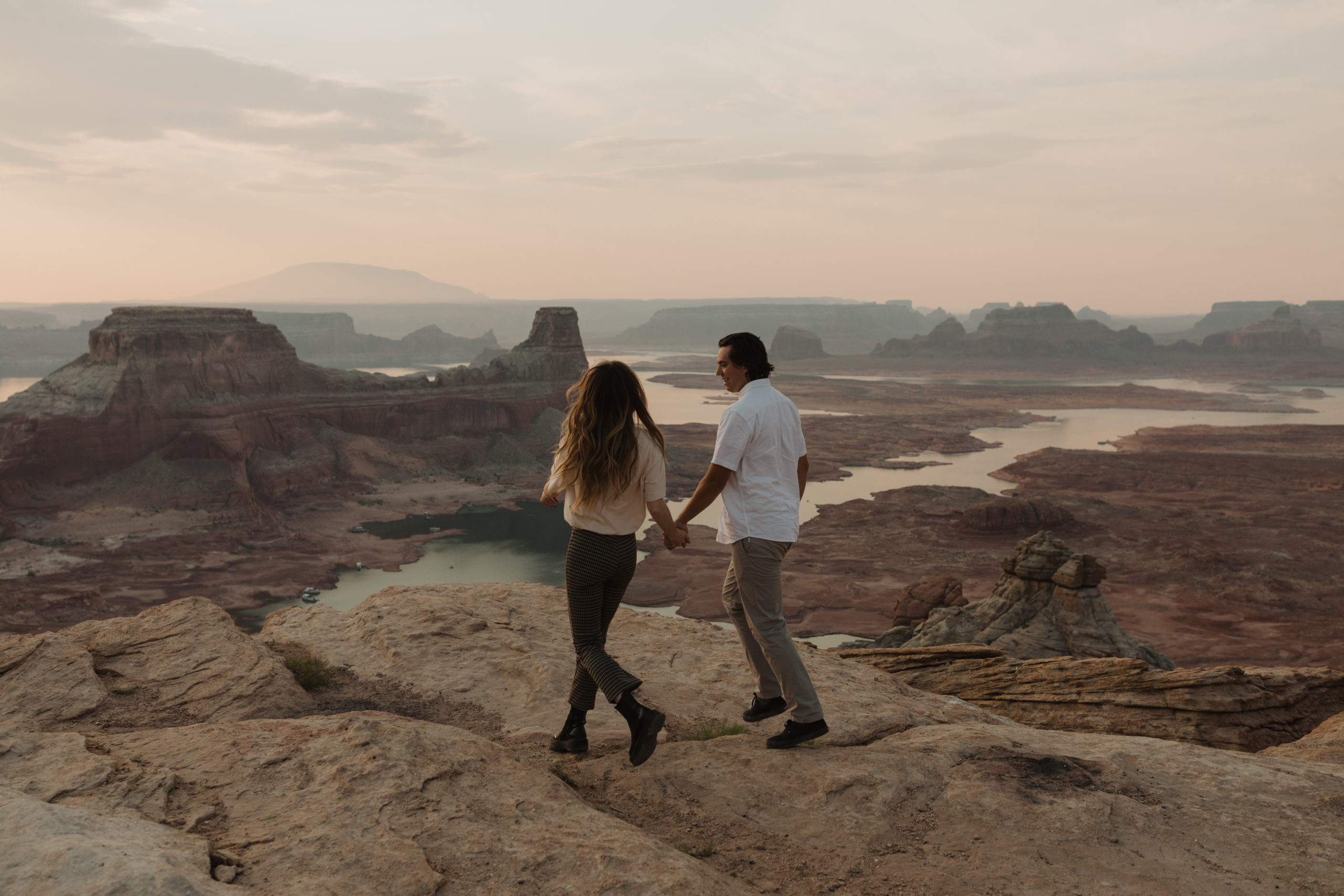 couple holds hands and walks at Alstrom Point above Lake Powell in Utah